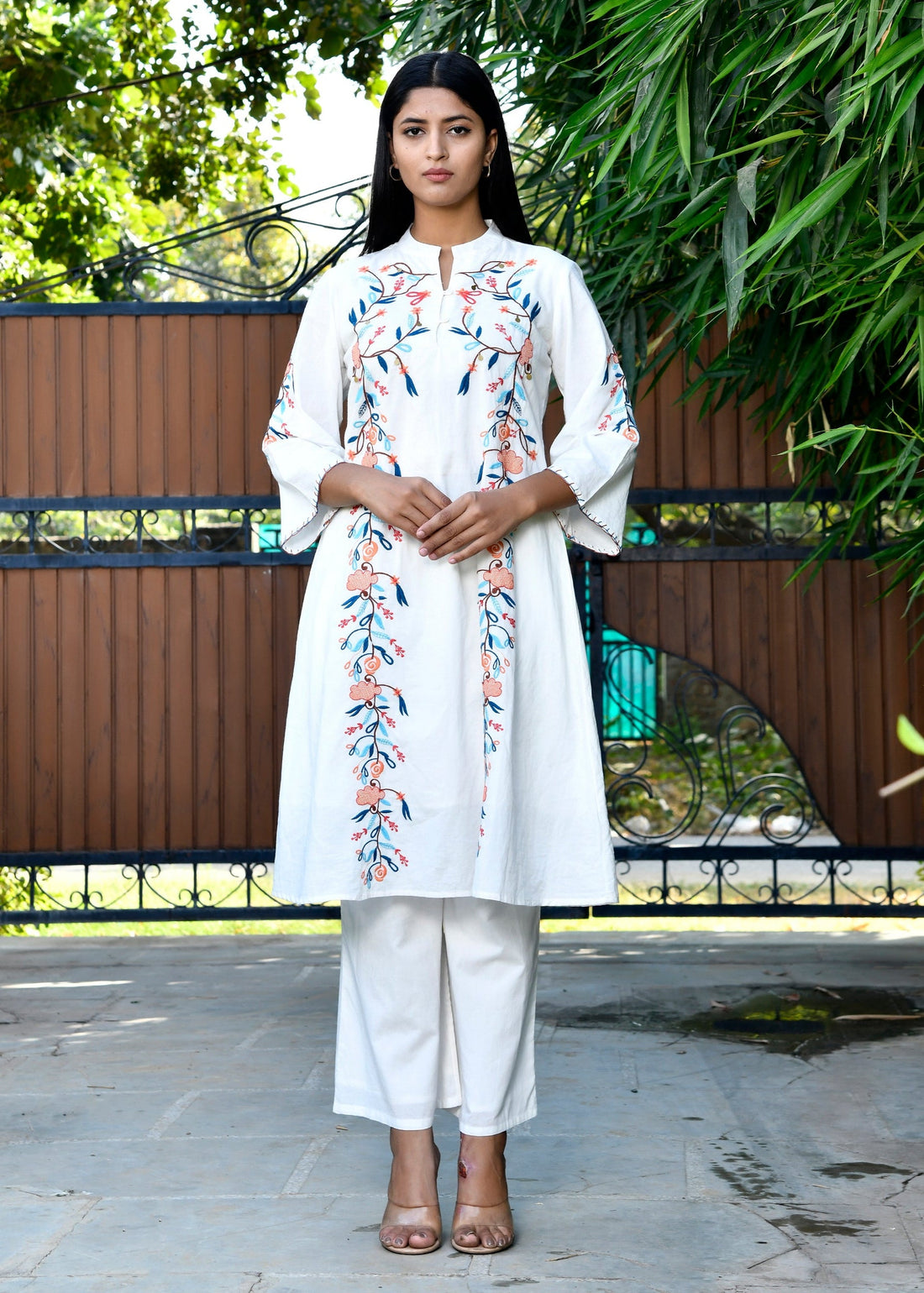 Woman wearing a white outfit with floral patterns standing outdoors.