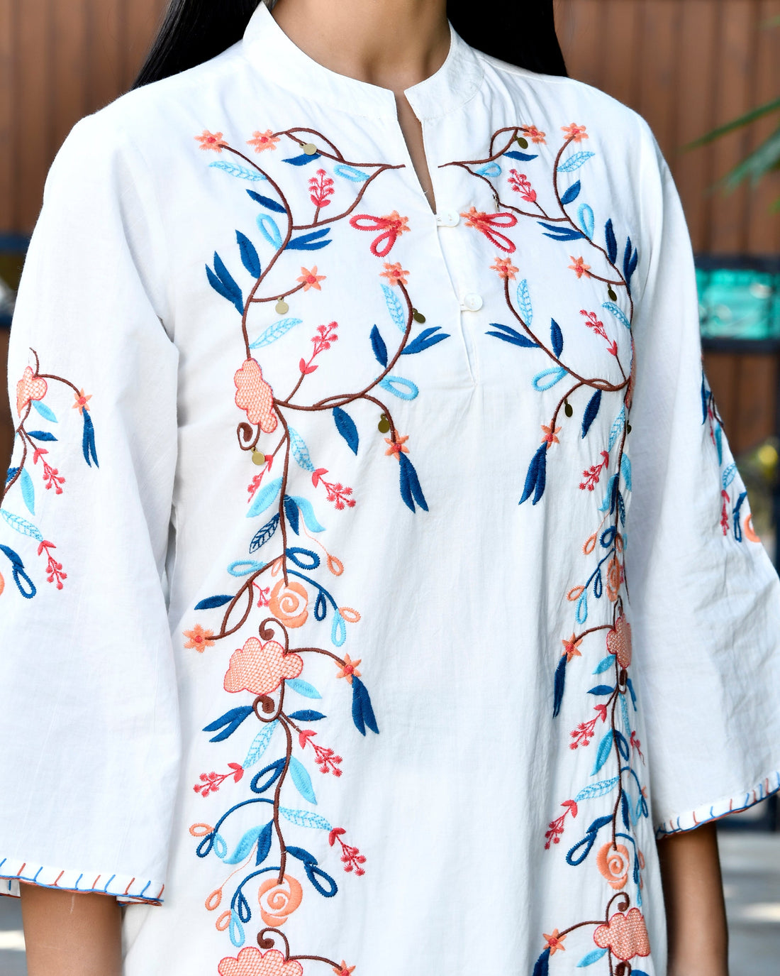 Woman wearing a white outfit with floral patterns standing outdoors.